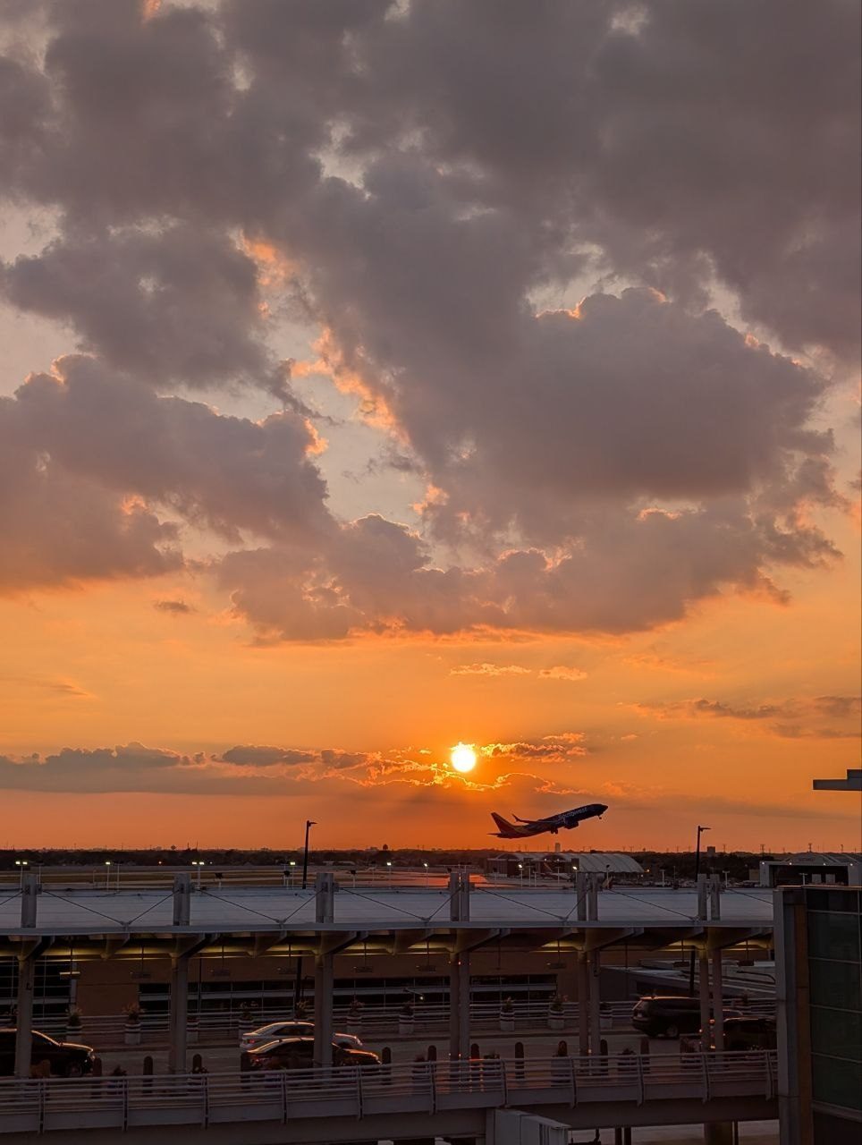 A Southwest 737 climbing out of Midway at sunset beneath a sky of orange and grey clouds, a light pole in the foreground