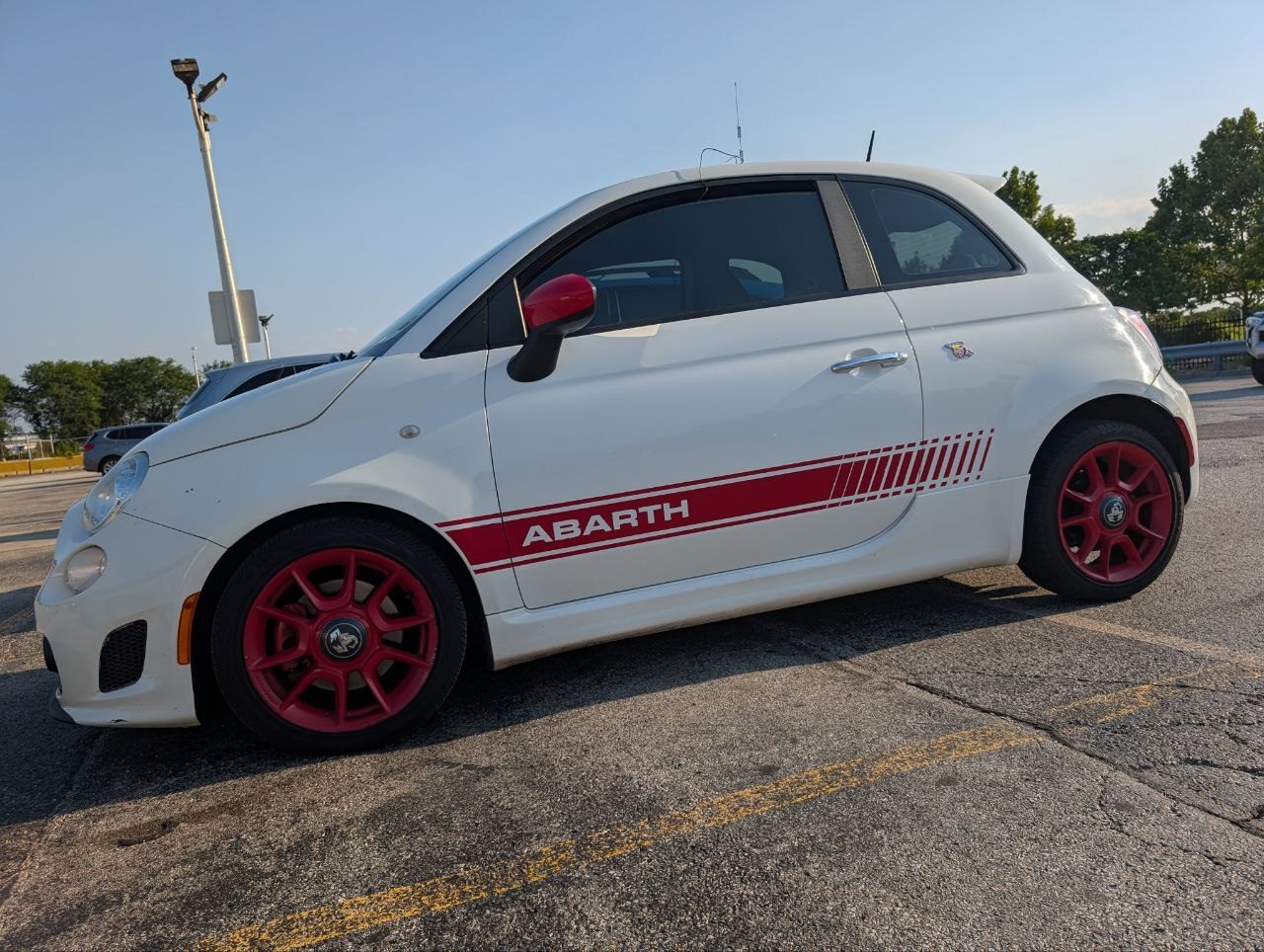 The white Abarth parked in the O’Hare cell phone lot with a small antenna on its roof under a hazy summer sky